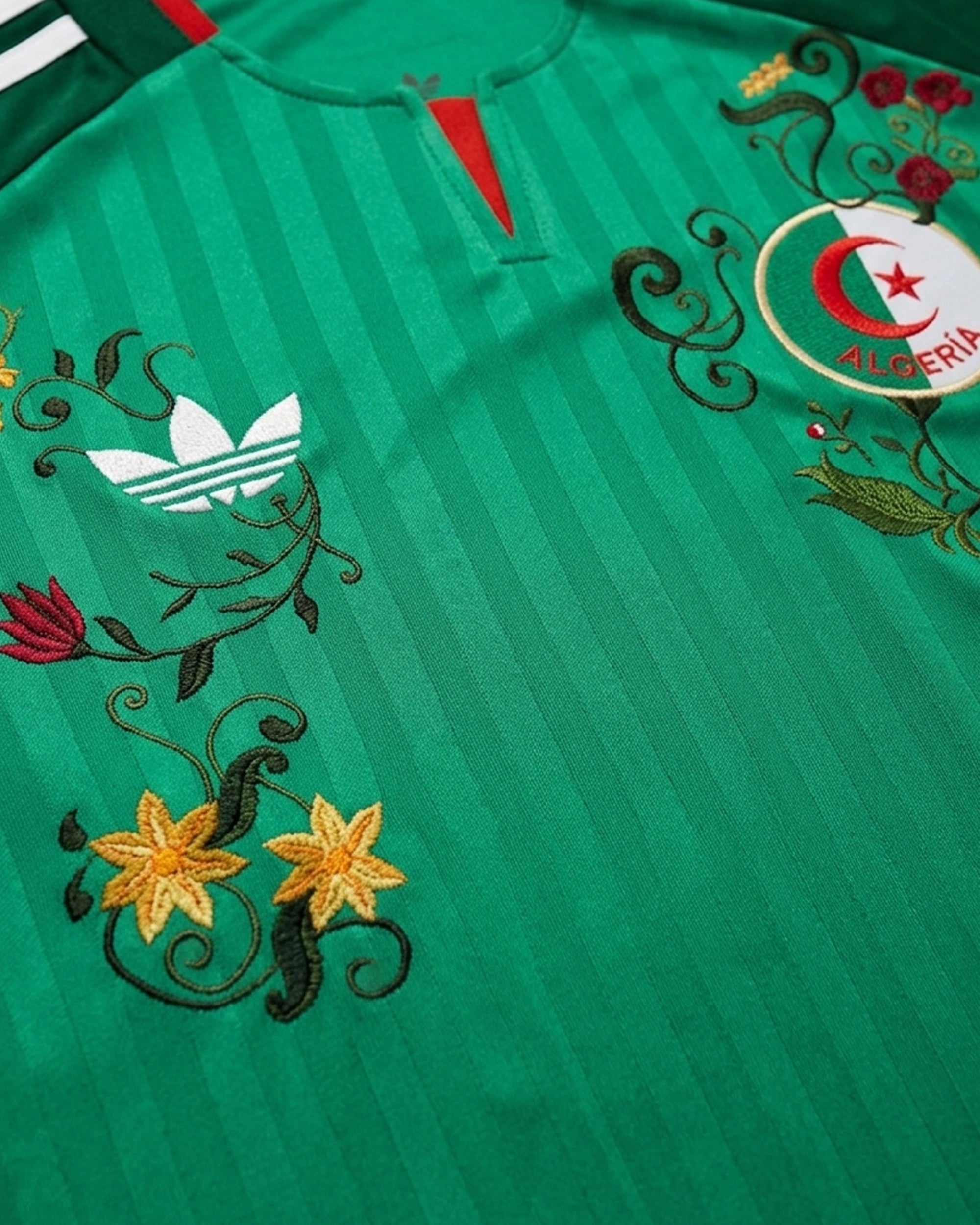 Close-up detail of the artisan embroidery on the right chest of the Algeria World Cup 2026 Jersey Reinvented, showcasing rich golden threads and deep red floral motifs hand-guided around the vintage Trefoil logo.
