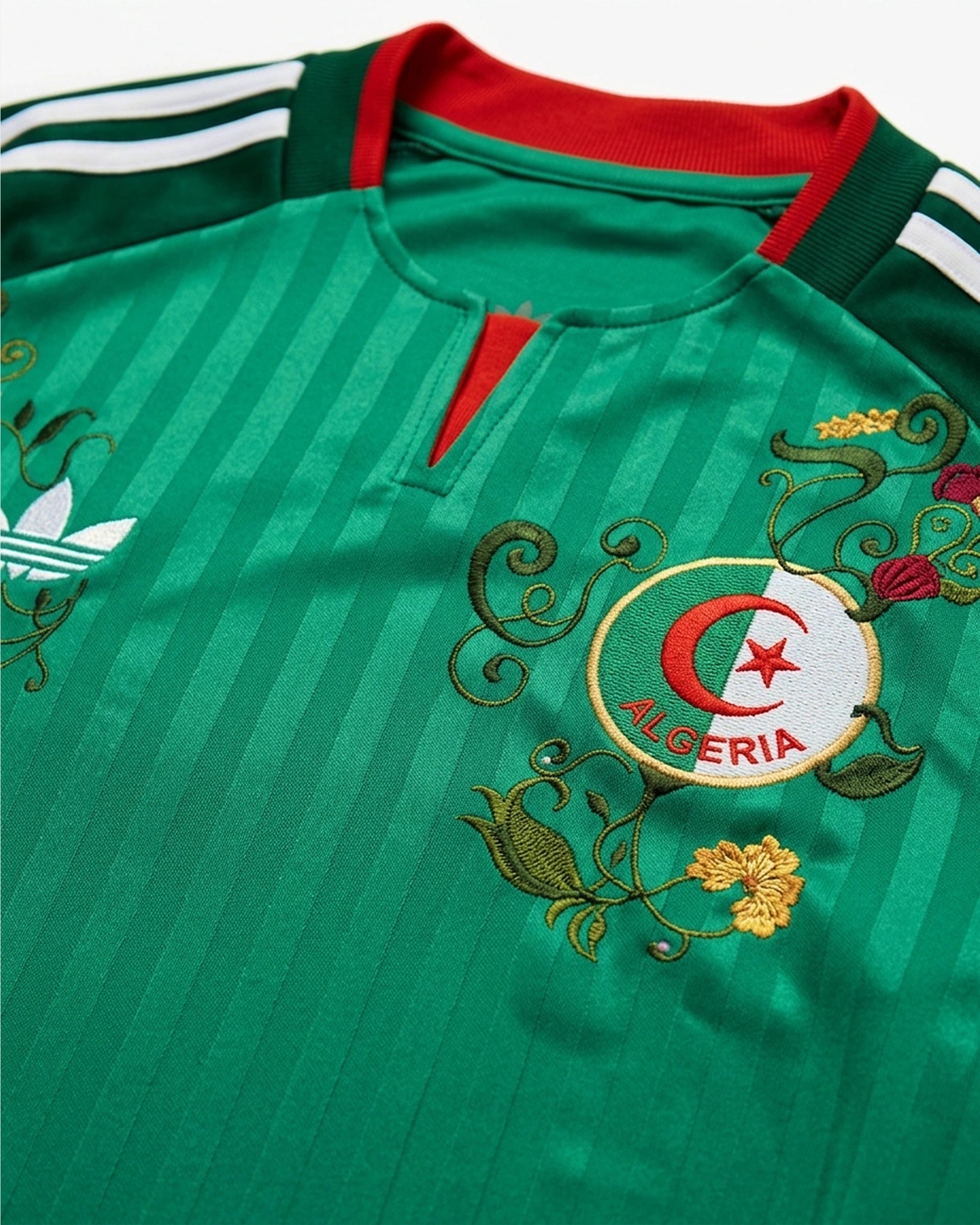 Close-up detail of the Algeria Embroidered Jersey crest, featuring intricate gold and red botanical stitching encircling the Algeria Football Federation badge, demonstrating haptic 3D texture.