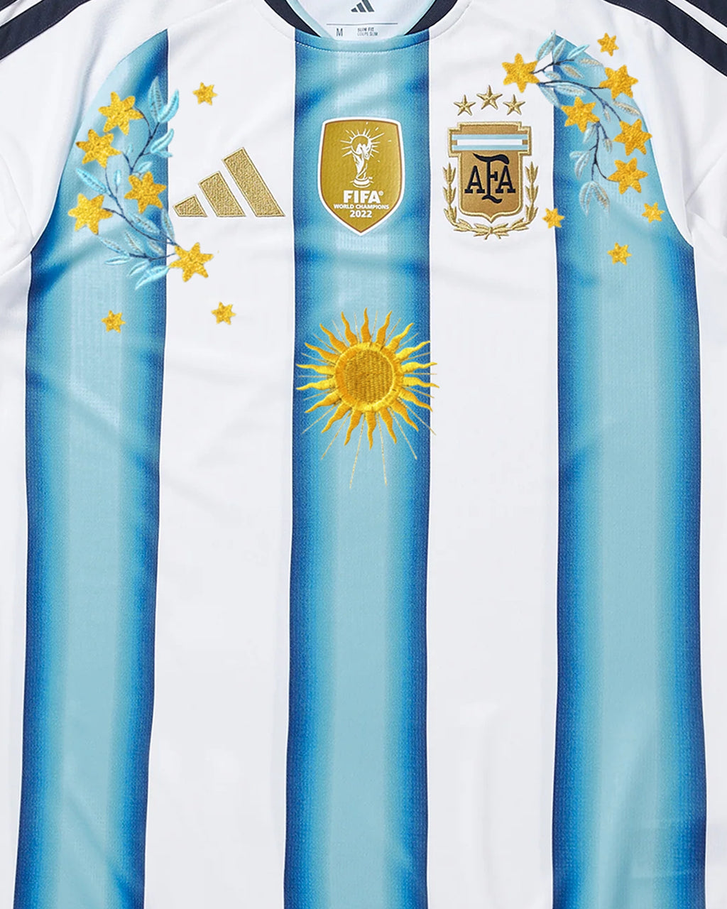 Hand-embroidered gold Sol de Mayo sun, scattered gold stars and laurel branch botanical art on Argentina 2026 home concept jersey — artisanal embroidery VOLTA Paris & Versailles