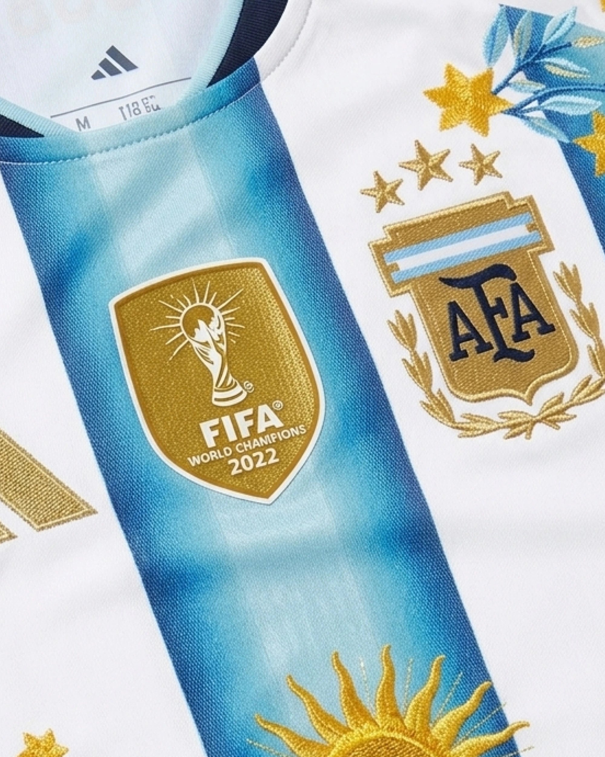 FIFA World Champions 2022 badge with gold hand-embroidered adidas stripes and gold star botanical wreath on Argentina 2026 albiceleste concept jersey — VOLTA Sol de Oro Edition