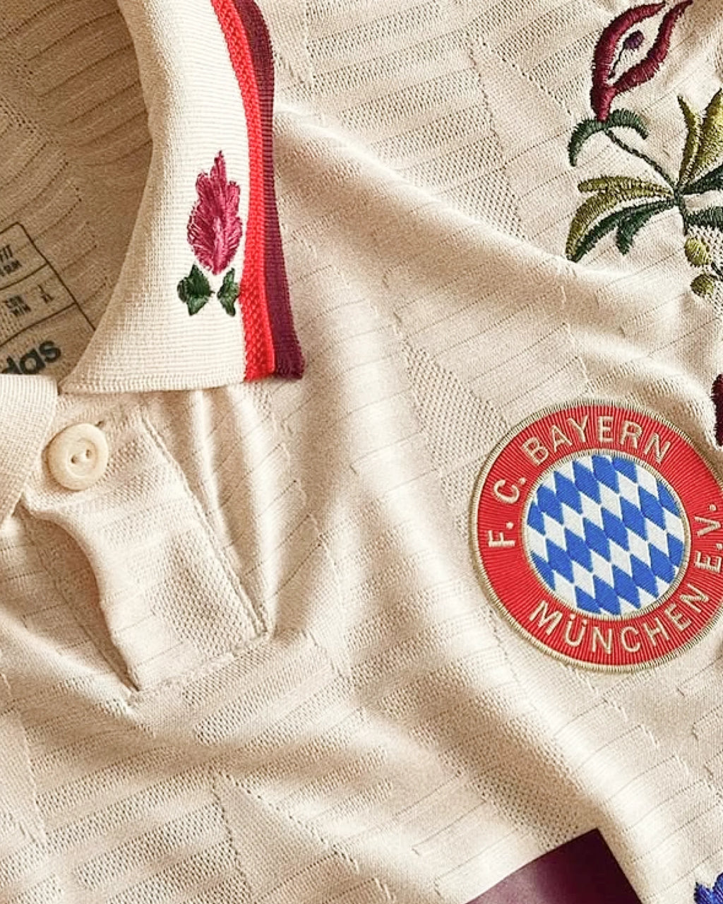 Bayern Munich badge and collar detail with hand-embroidered pink rose on sleeve — folk botanical embroidery on authentic cream base — VOLTA Bavarian Folk Edition Paris & Versailles