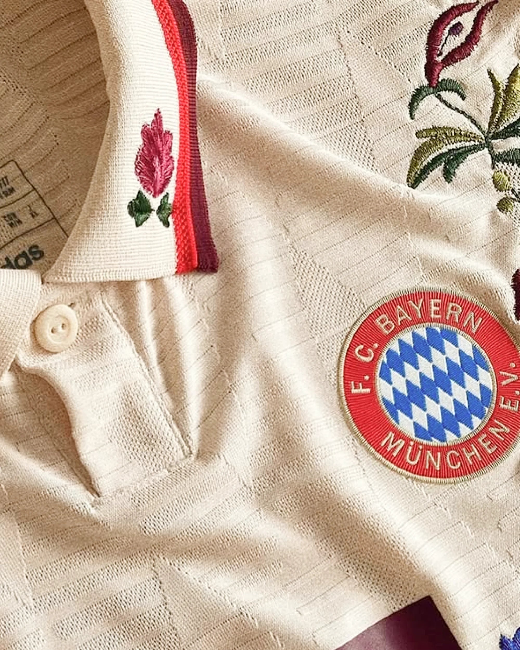 Bayern Munich badge and collar detail with hand-embroidered pink rose on sleeve — folk botanical embroidery on authentic cream base — VOLTA Bavarian Folk Edition Paris & Versailles