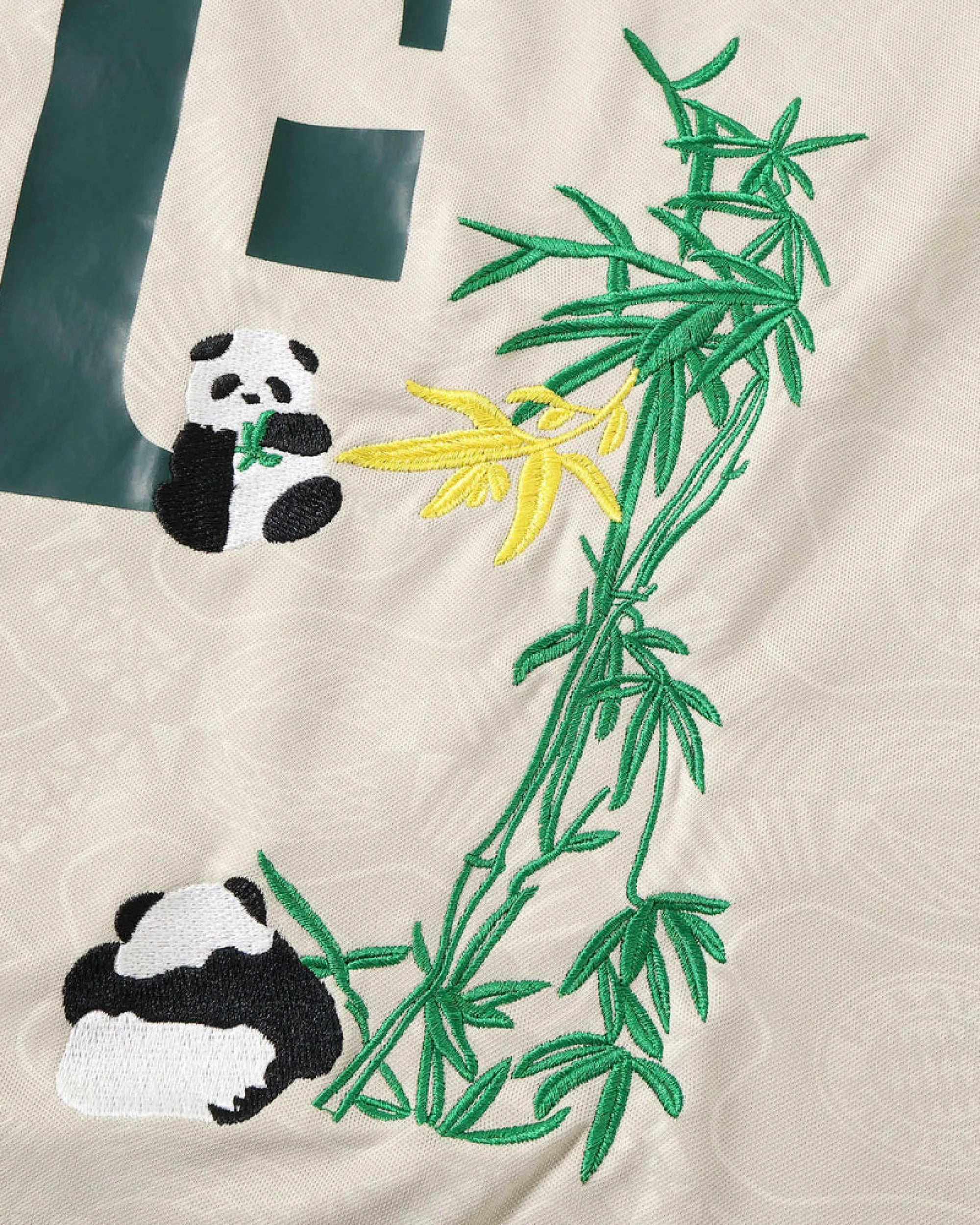 Close-up hand-embroidered giant panda cub resting under bamboo branches on Bayern Munich stone beige concept jersey — artisanal embroidery VOLTA Paris & Versailles