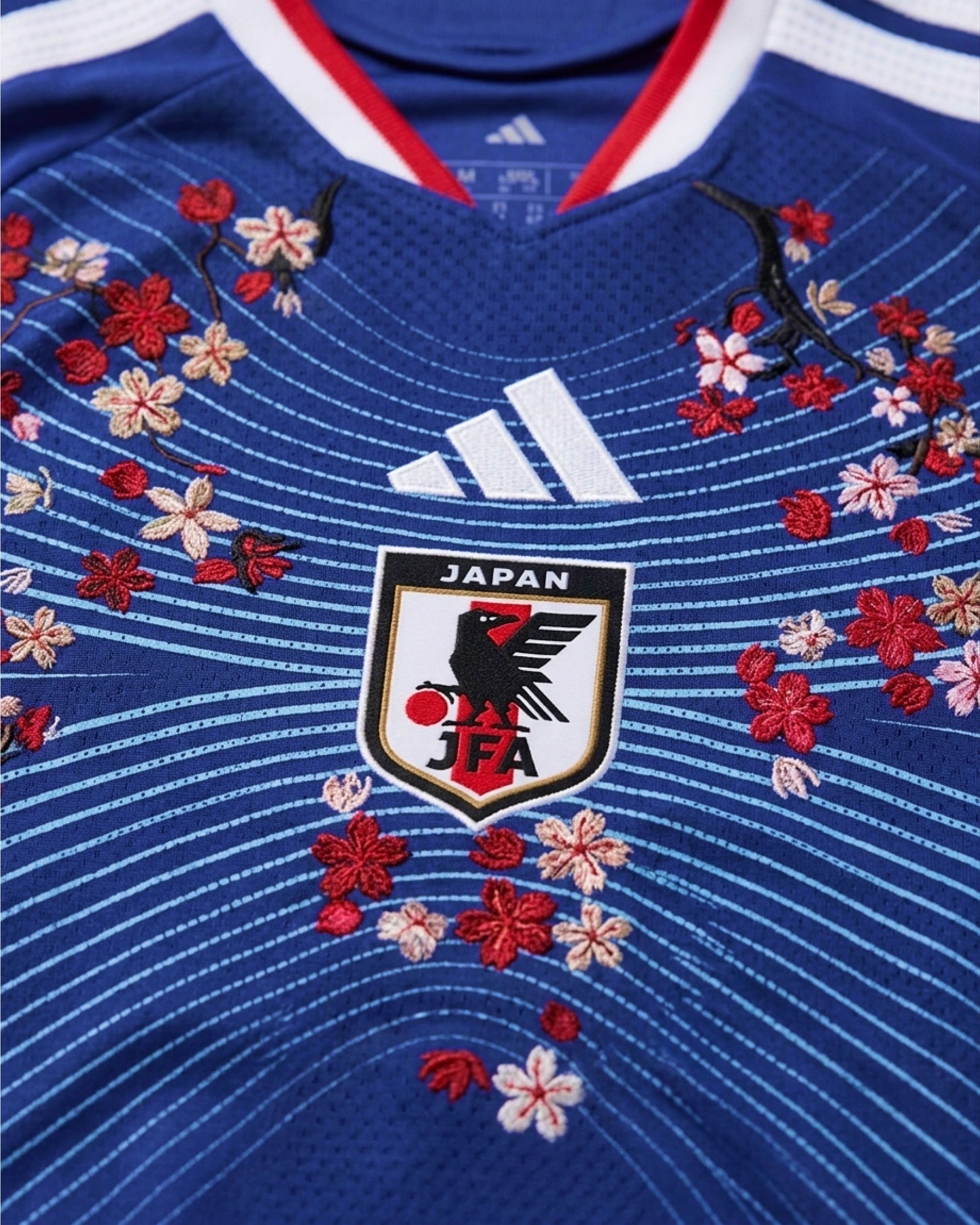 Macro detail of the authentic, limited-edition gold and white 'Volta Football Collective' badge stitched onto the left hem of the Japan Embroidered Jersey.