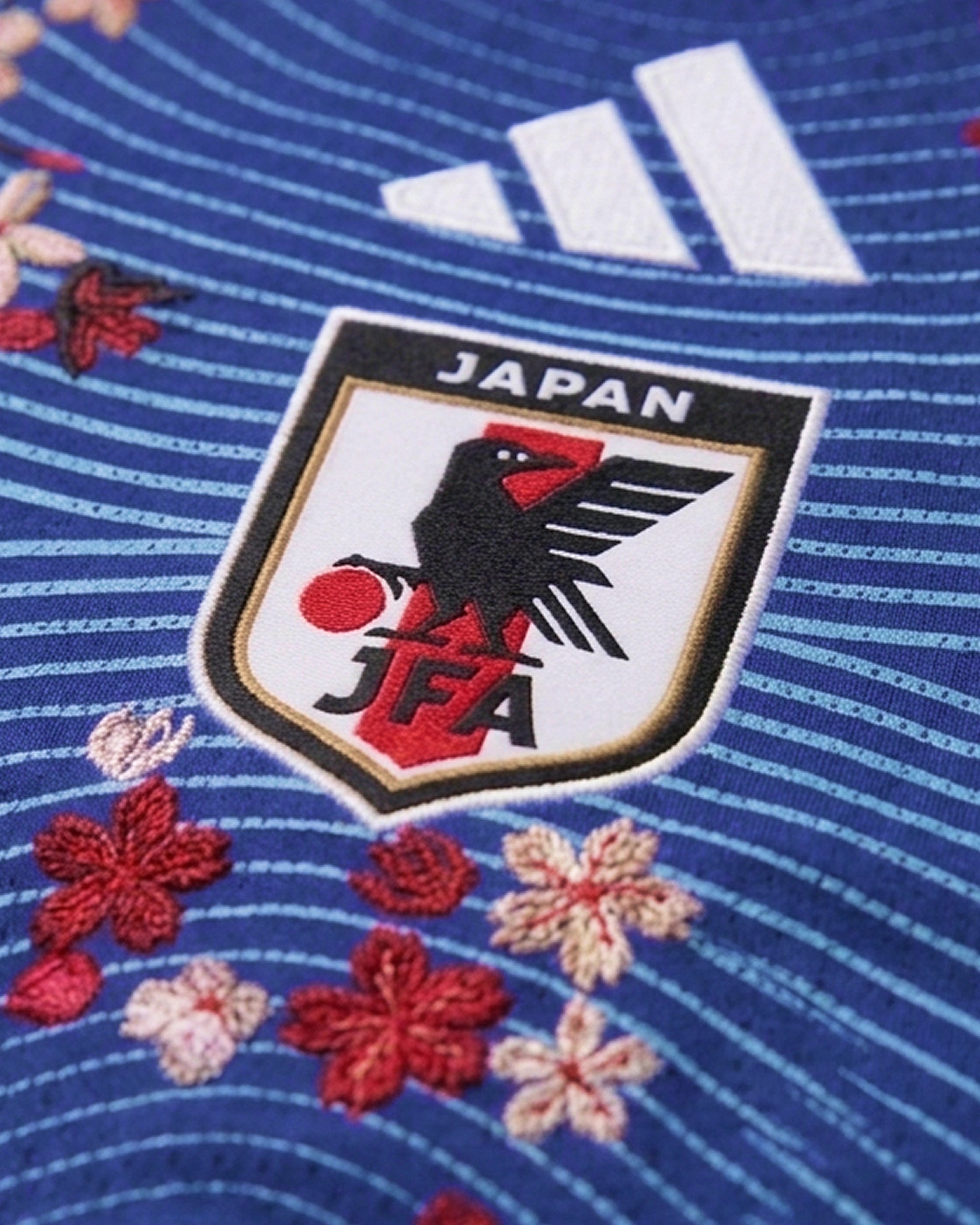 Macro detail of the hand-guided gold botanical embroidery on the right chest of the Japan World Cup Jersey Revisited, highlighting the haptic texture of the threads.