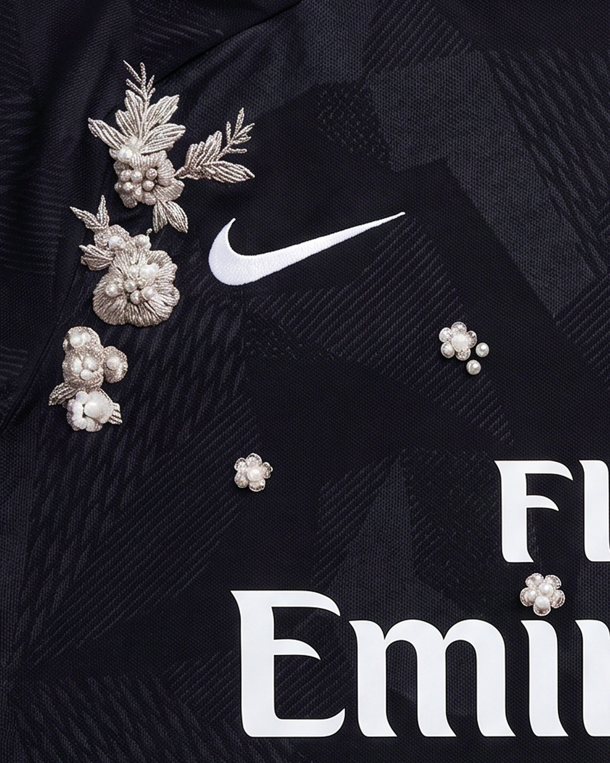Close-Up Macro Detail Of the Paris Embroidered Black Jersey Crest, Highlighting The High-Density Silver Thread Flowers and Pearl Accents Framing The Circular Team Emblem.