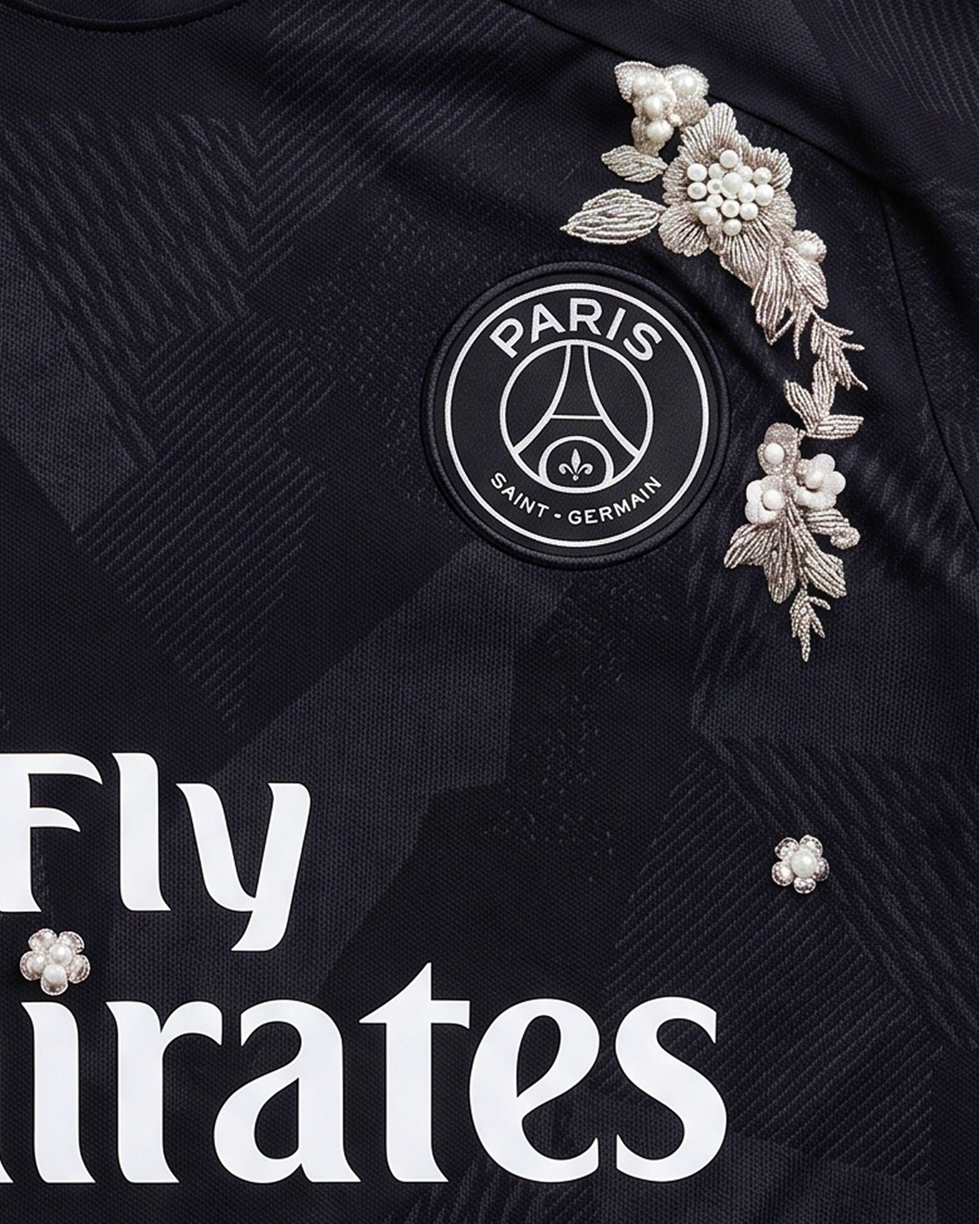 Macro Texture Shot Of The Right Chest On The Paris Retro Shirt Revisited, Showcasing Elegant Hand-Guided Silver Leaf Stitching and Scattered Ivory Pearls Floating Around The White Brand Swoosh.