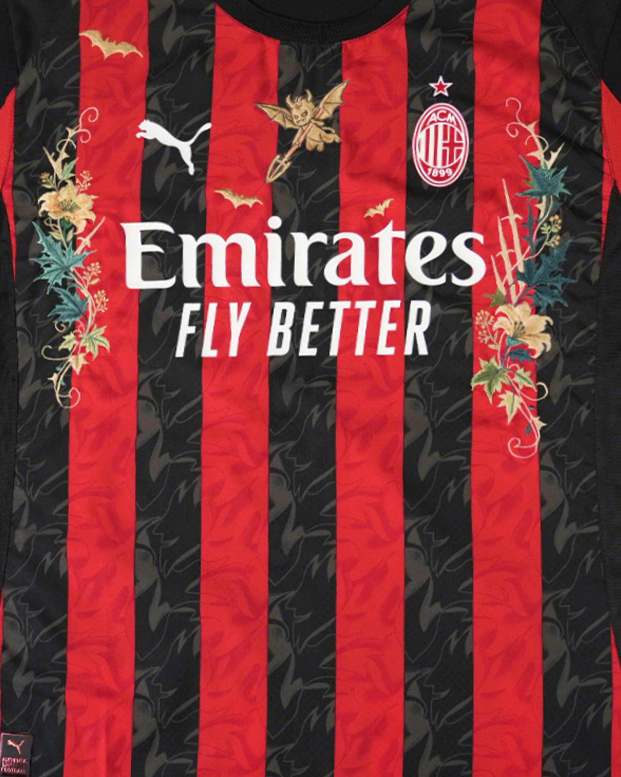 Medium Chest Shot Detail Of The AC Milan 2024/25 Jersey Reimagined, Showcasing Golden Devil, Bat, And Green Thistle Embroidery Winding Symmetrically Around The Sponsor.