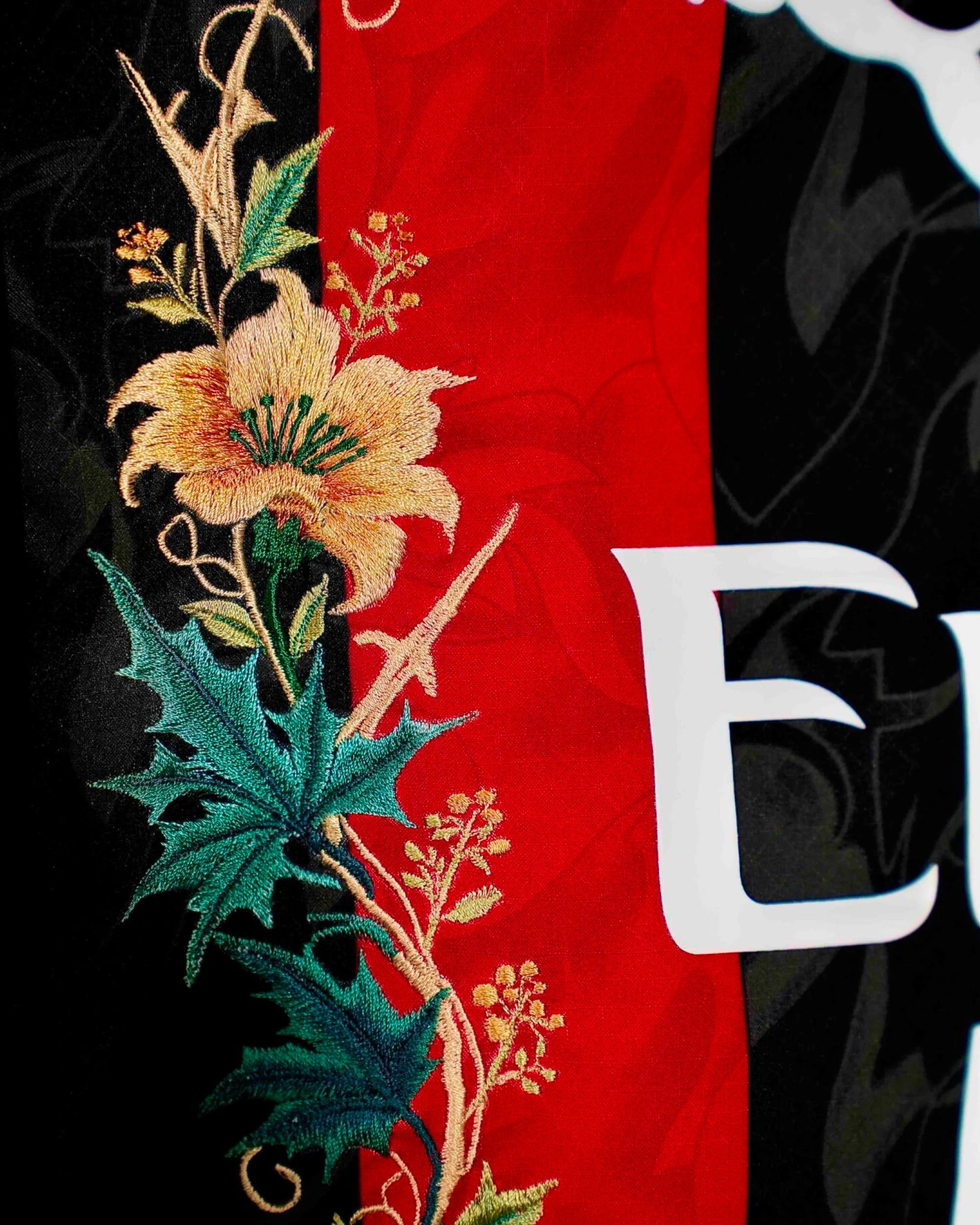 Macro Detail Focusing On The Right Side Panel Leaf Stitches, Showcasing Premium Multitonal Green and Ivory Thread Gradients Over the Red Fabric Stripe.