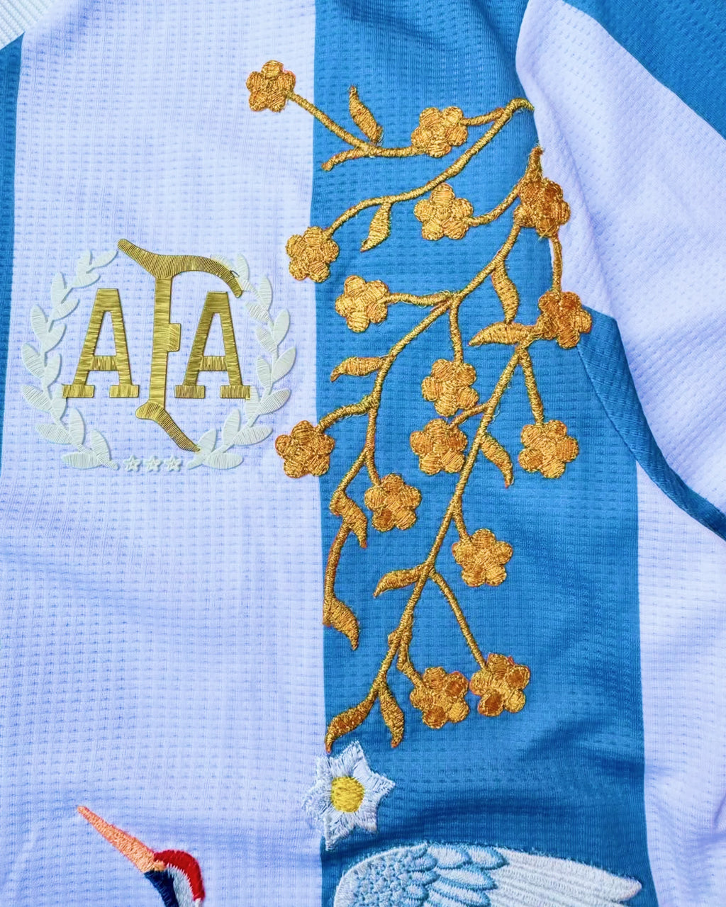 Close-up hand-embroidered soaring crane and teal wave botanical art on Argentina albiceleste concept jersey — artisanal embroidery Paris & Versailles — VOLTA Albiceleste Rising Edition