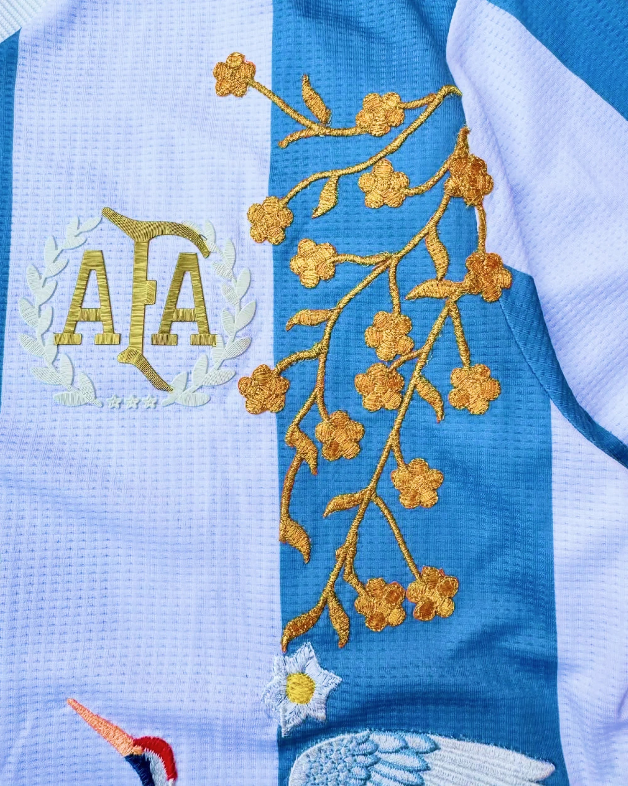 Close-up hand-embroidered soaring crane and teal wave botanical art on Argentina albiceleste concept jersey — artisanal embroidery Paris & Versailles — VOLTA Albiceleste Rising Edition