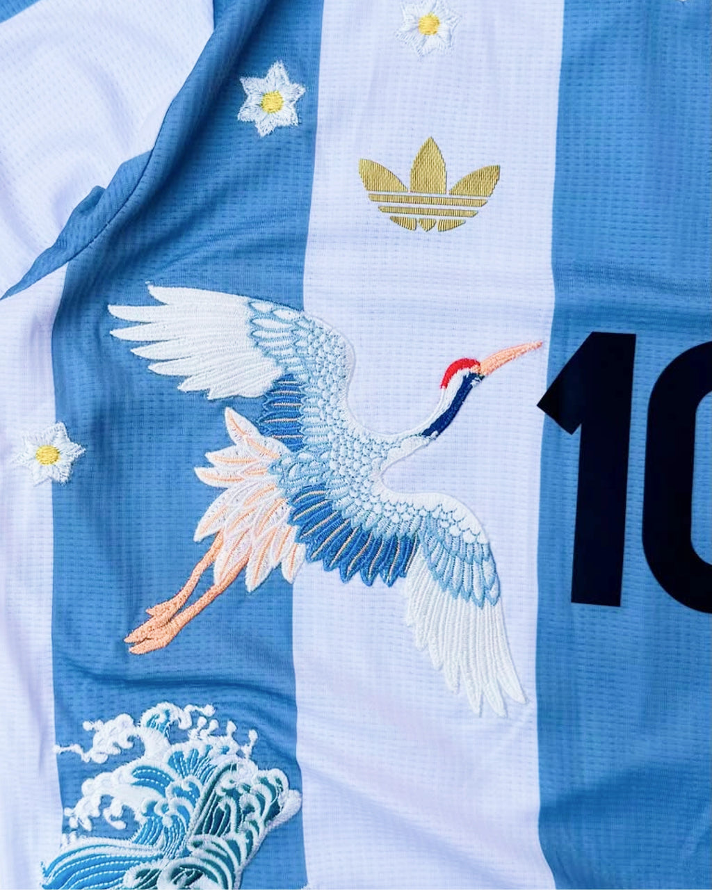 AFA badge detail with hand-embroidered golden botanical flower branches cascading on Argentina albiceleste concept jersey — limited edition VOLTA Paris & Versailles