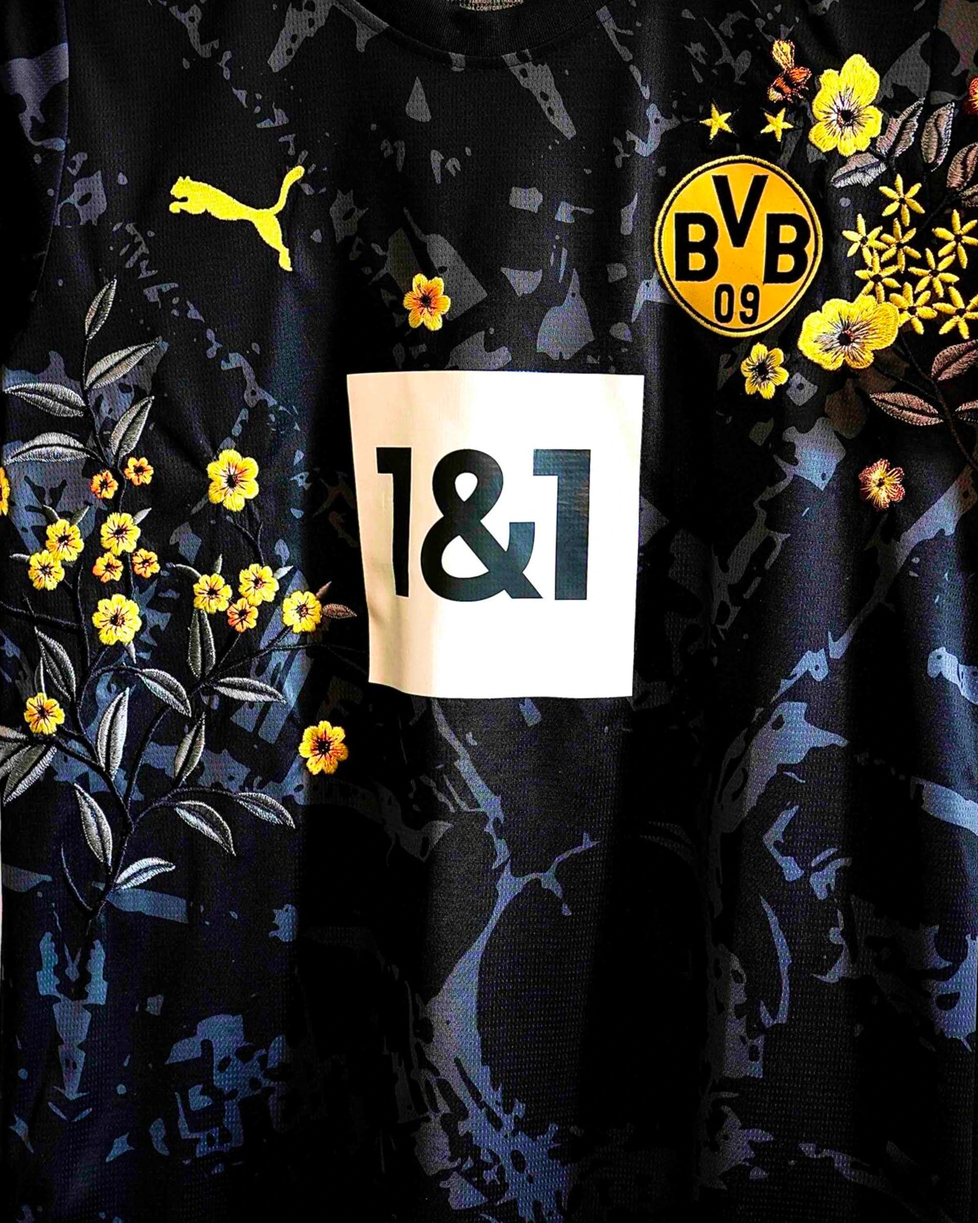 Medium Chest Shot Detail Of The Borussia Dortmund Concept Jersey, Showcasing Symmetrical Yellow Primrose Embroidery Framing The Central White Sponsor Block.