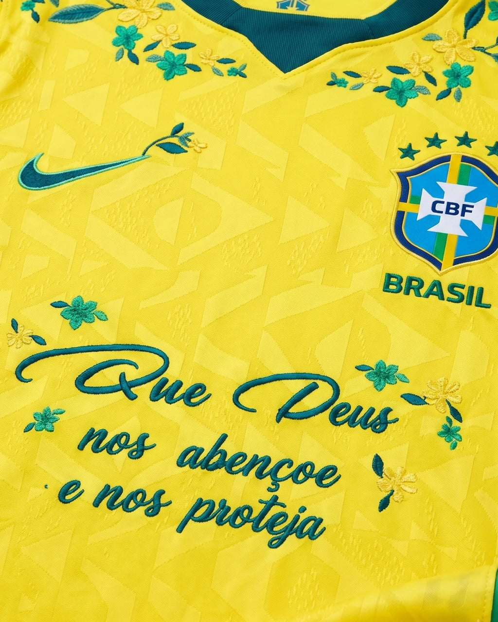 Hand-embroidered faith inscription "Que Deus nos abençoe e nos proteja" with teal and yellow botanical flowers on Brazil World Cup 2026 concept jersey — artisanal embroidery VOLTA Paris & Versailles