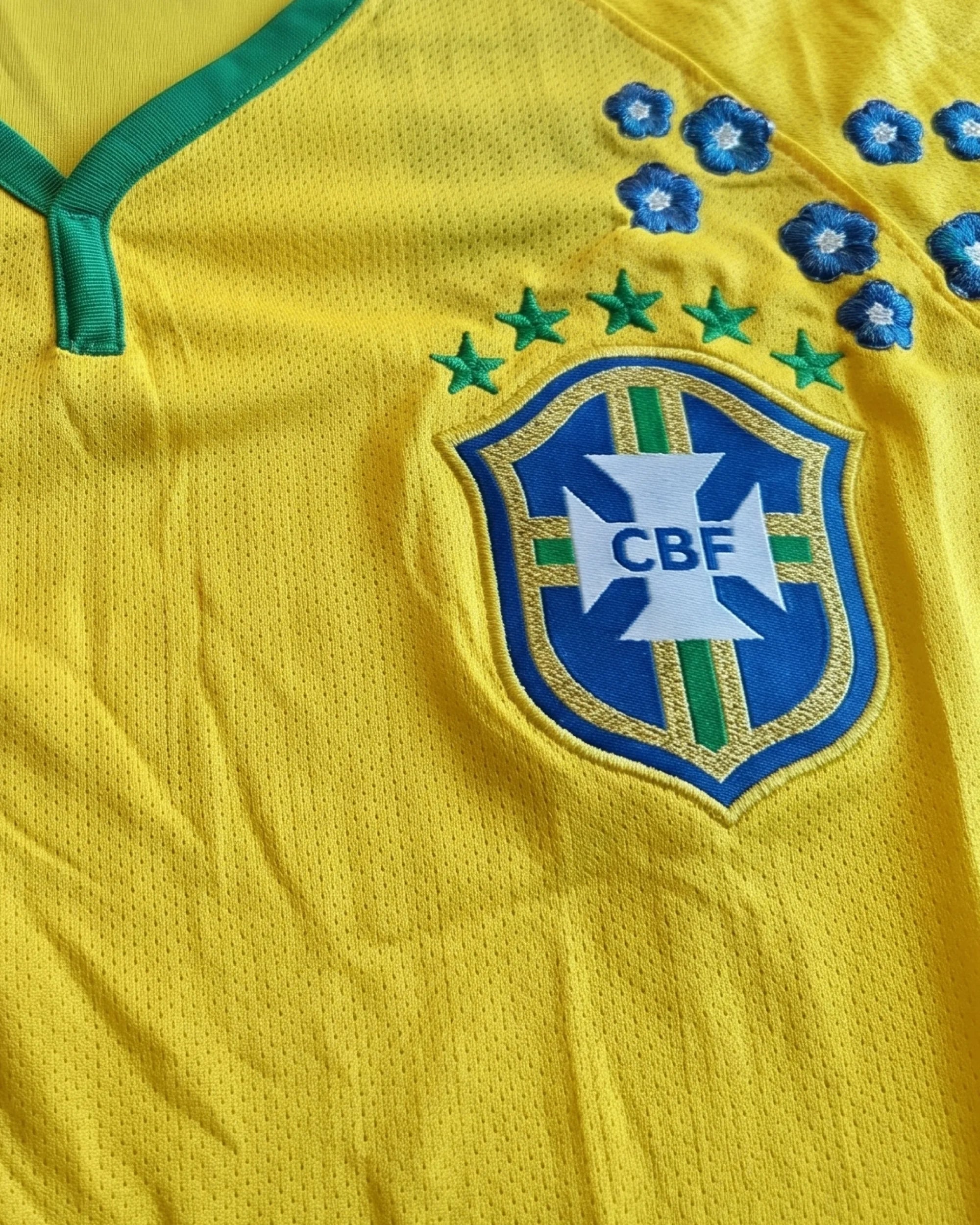Close-Up Detail Of The Brazil Embroidered Jersey Crest Illustrating High-Density Indigo Blue Floral Embroidery Adorning The Five-Star National Emblem.