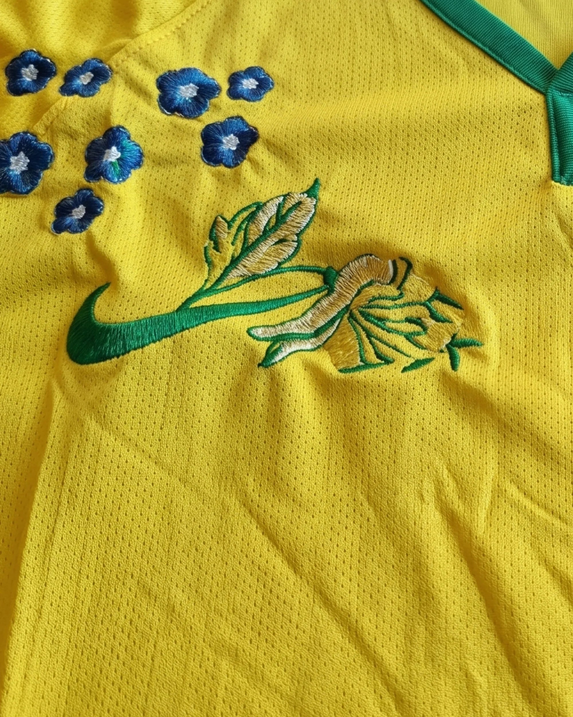 Macro Texture Shot Of The Brazil Embroidered Kit Chest Highlighting Green And Yellow Botanical Leaves Stitched Seamlessly Over The Brand Logo.