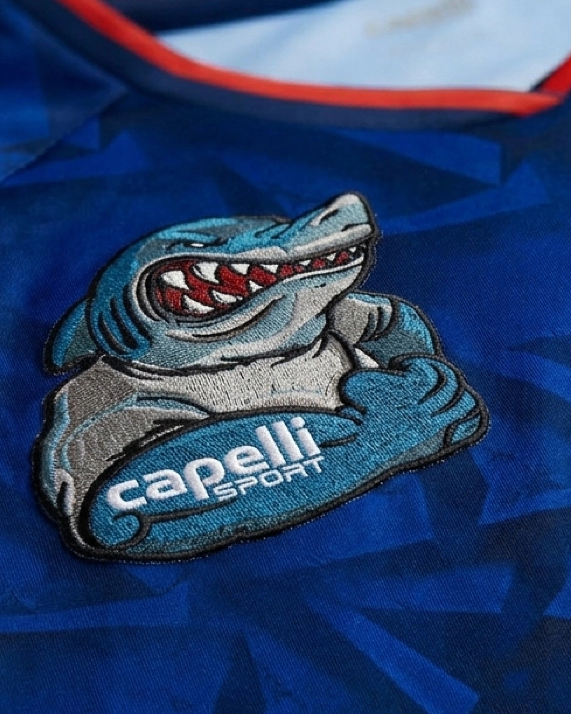 Detailed view of hand-embroidered Cape Verde shark mascot with arms crossed and red teeth — VOLTA Paris