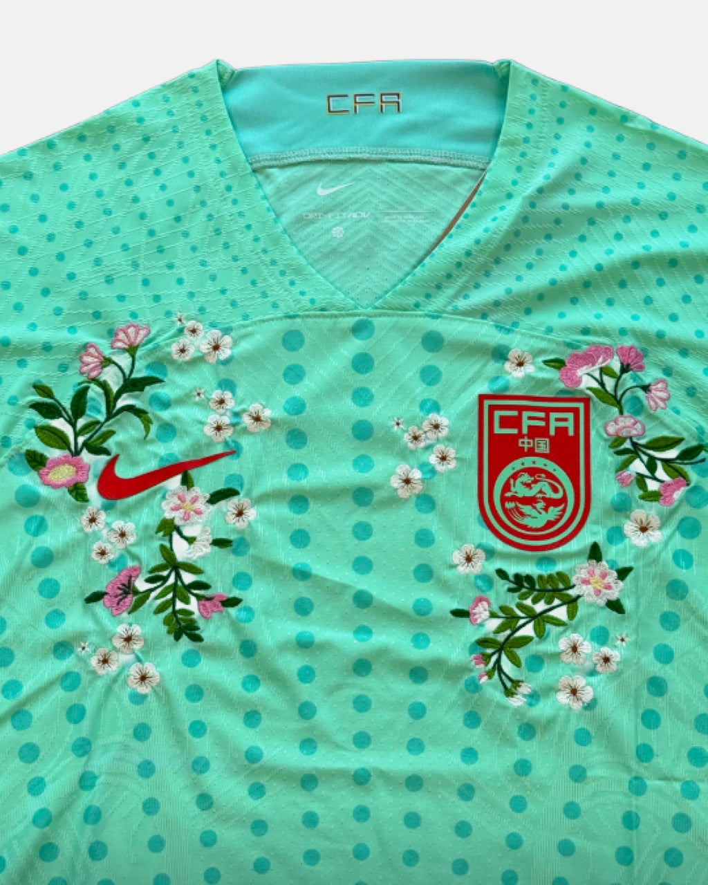 Close-up hand-embroidered cherry blossom and peach flower wreath surrounding CFA badge on China concept jersey — botanical embroidery Paris & Versailles — VOLTA