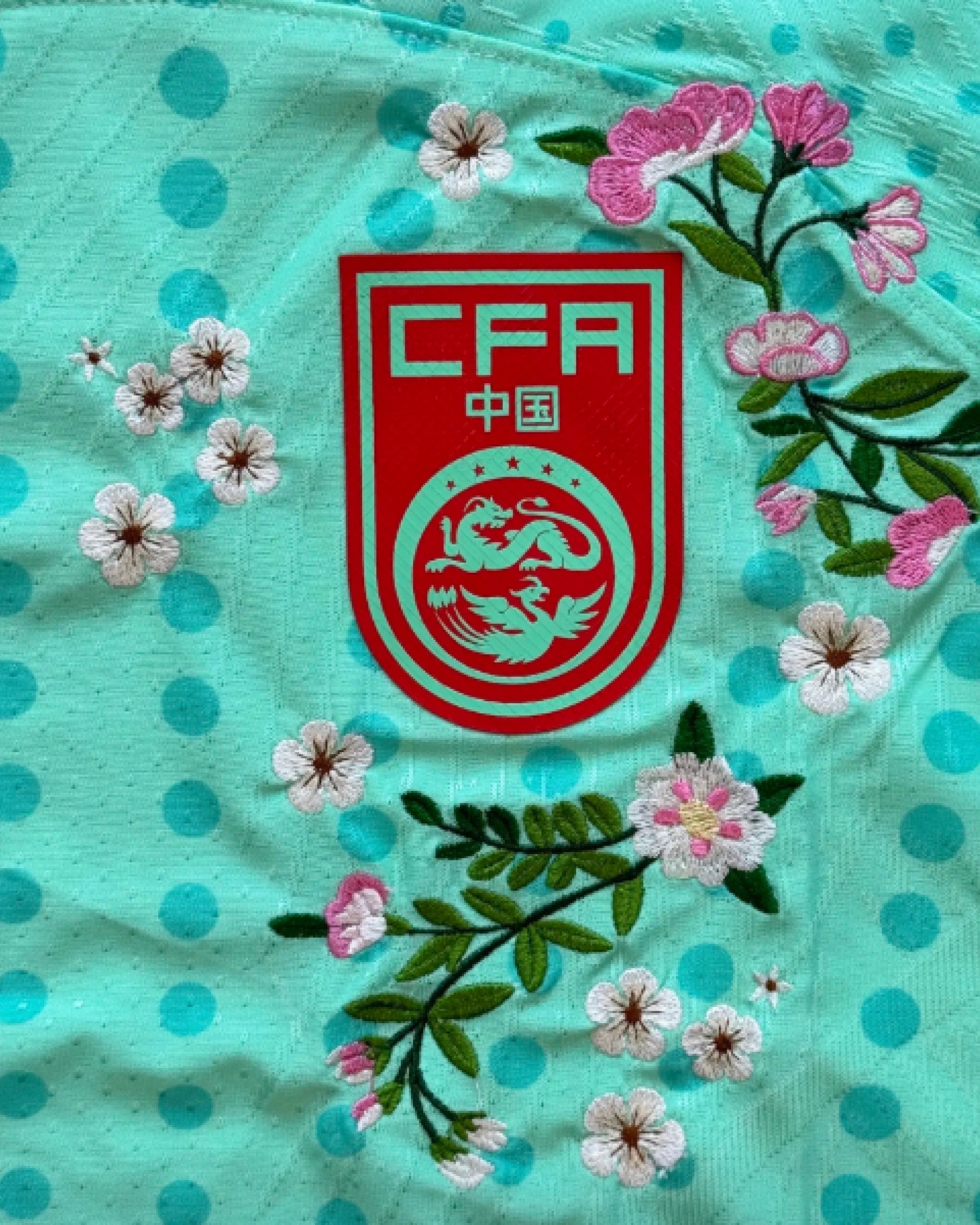 CFA China badge detail with hand-embroidered cherry blossoms and pink botanical flowers — custom China green embroidered jersey — VOLTA Dragon Blossom Edition