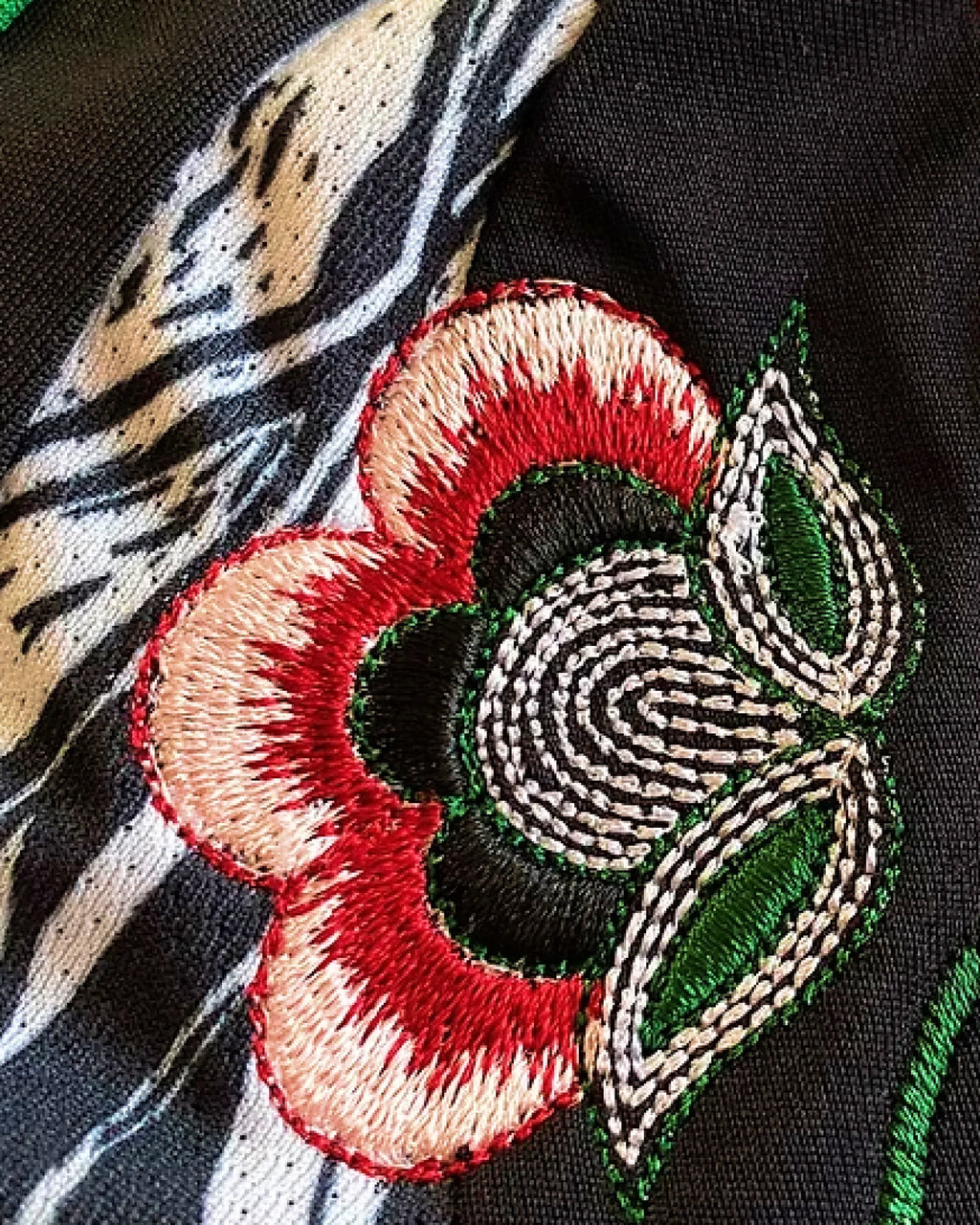 Close-Up Detail Of The Right Chest On the Arsenal Away Kit Revisited, Illustrating Intricate Ivory And Crimson Blossom Embroidery Framing The Green Brand Performance Logo.