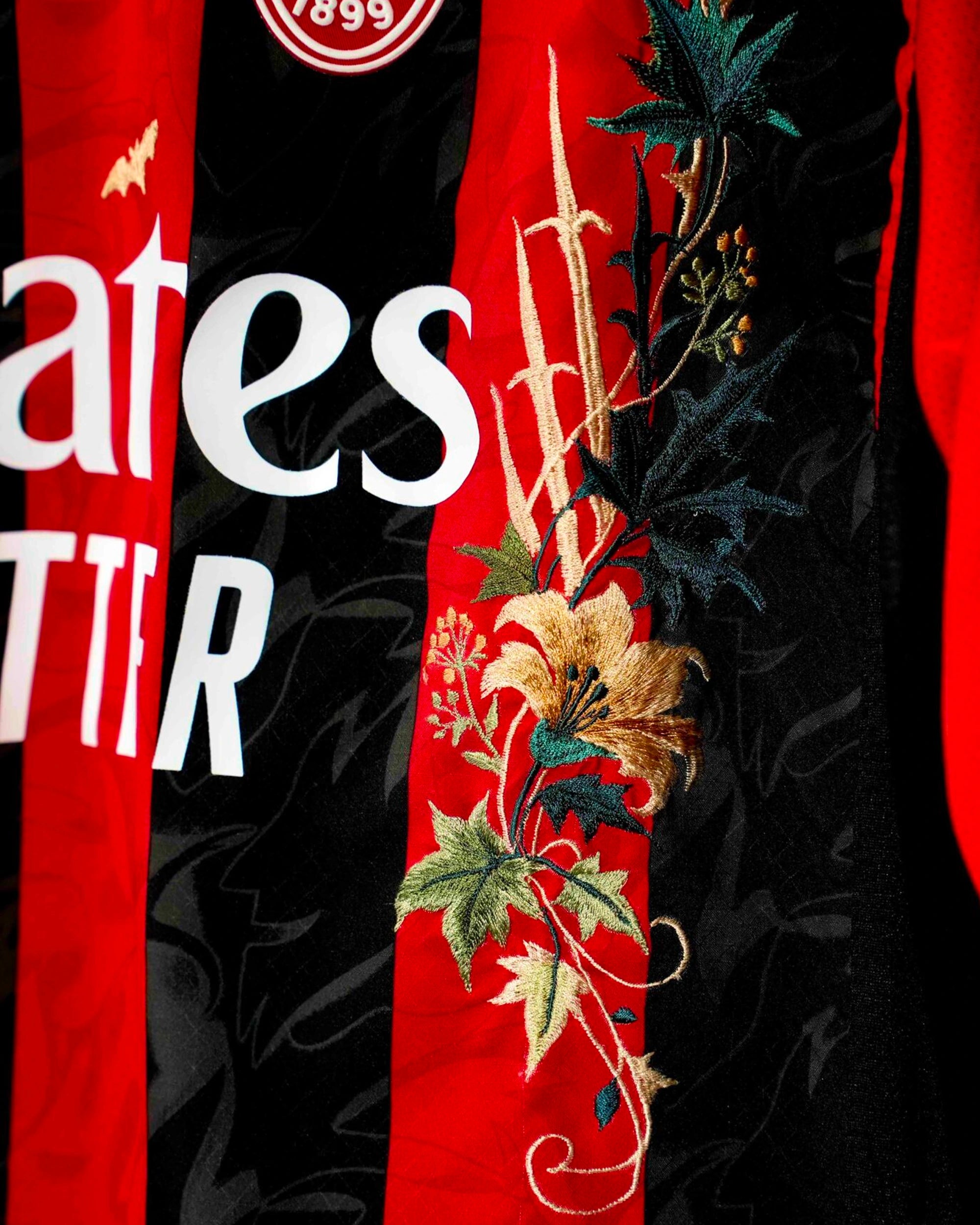 Macro Texture Shot Focusing On The Left Torso Border Of The Custom Embroidered Black Red Milan Shirt, Highlighting Textured Gold Flowers and Deep Green Ivy Leaves.