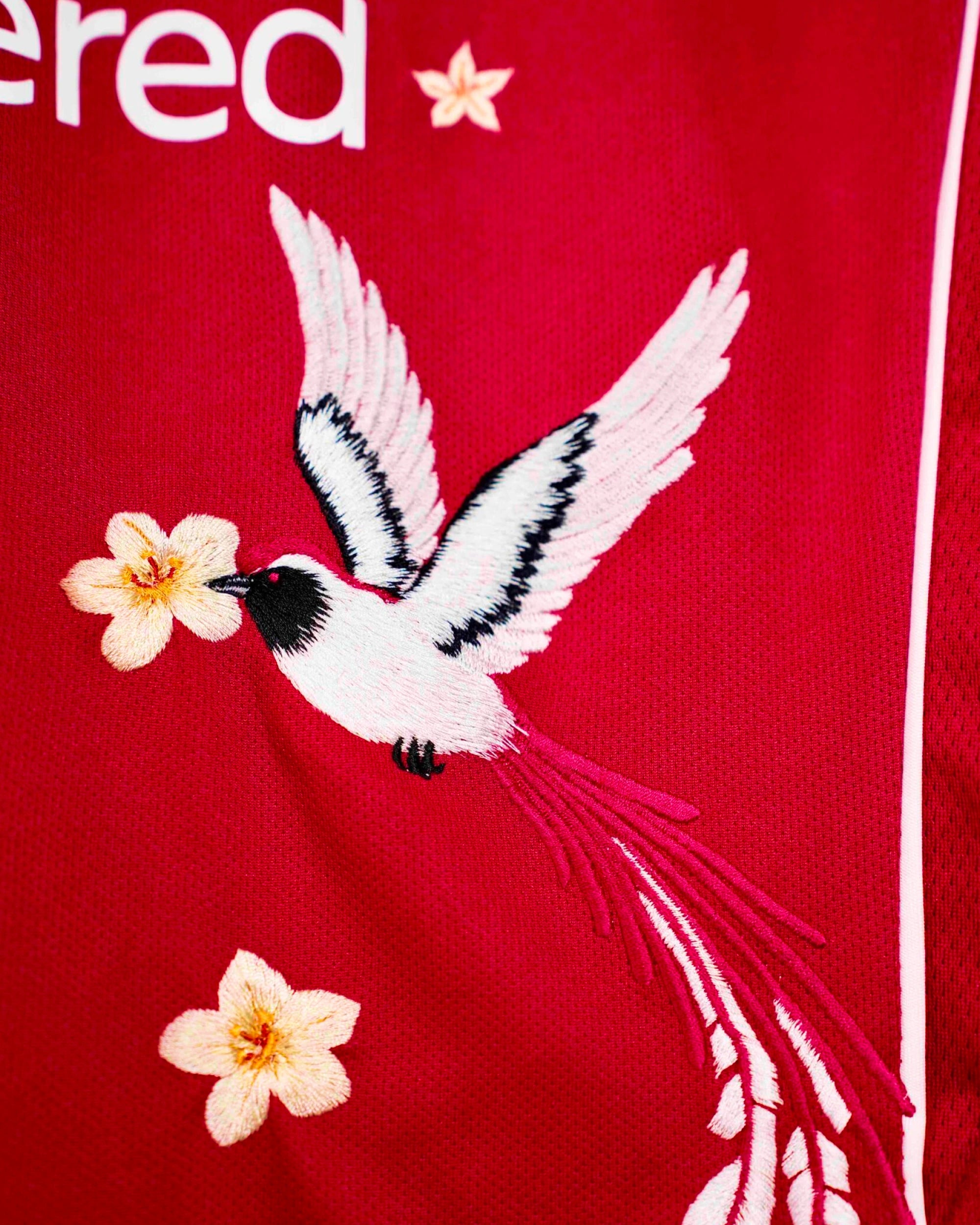 Macro Texture Shot Focusing On The Lower Right Torso Of The Custom Embroidered Red Liverpool Shirt, Showcasing The Haptic 3D Plume Stitches Of A Flying White Bird.