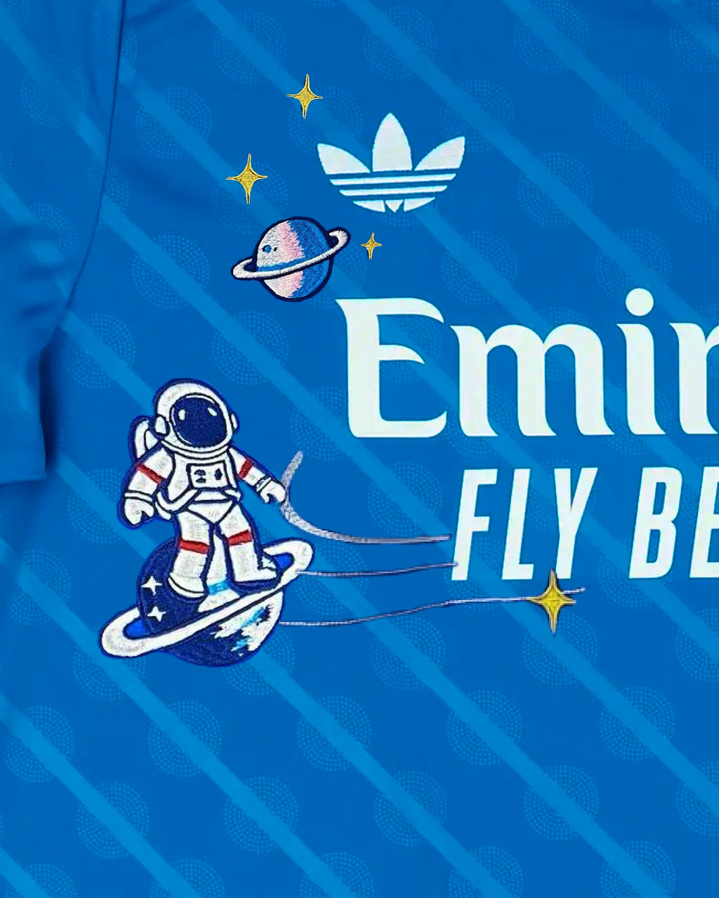 Macro Texture Shot On The Right Chest Of The Custom Embroidered Royal Blue Real Madrid Shirt, Showcasing Elegant Hand-Guided Vintage Astronaut Art Stitched Beneath the White Brand Logo.