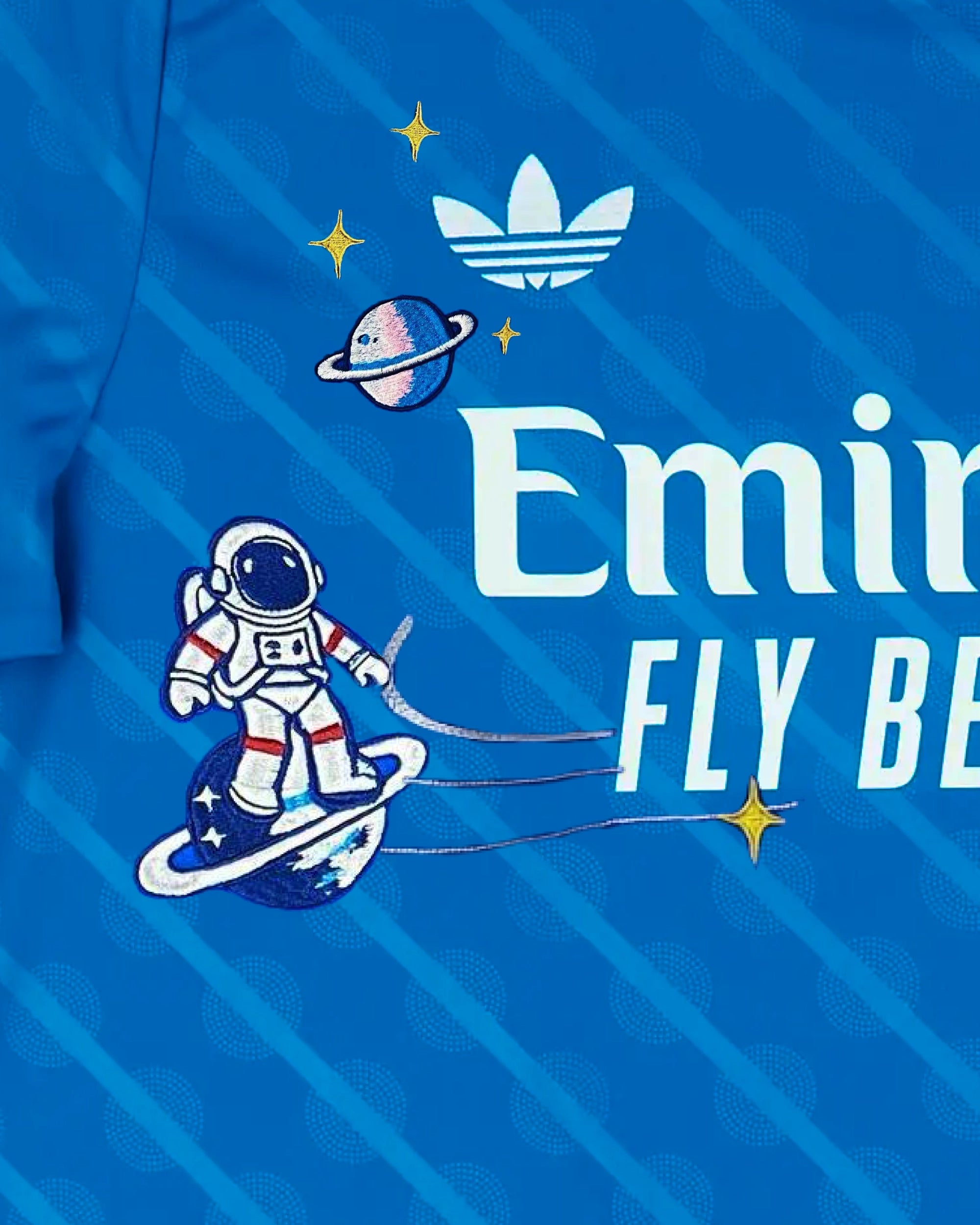 Macro Texture Shot On The Right Chest Of The Custom Embroidered Royal Blue Real Madrid Shirt, Showcasing Elegant Hand-Guided Vintage Astronaut Art Stitched Beneath the White Brand Logo.