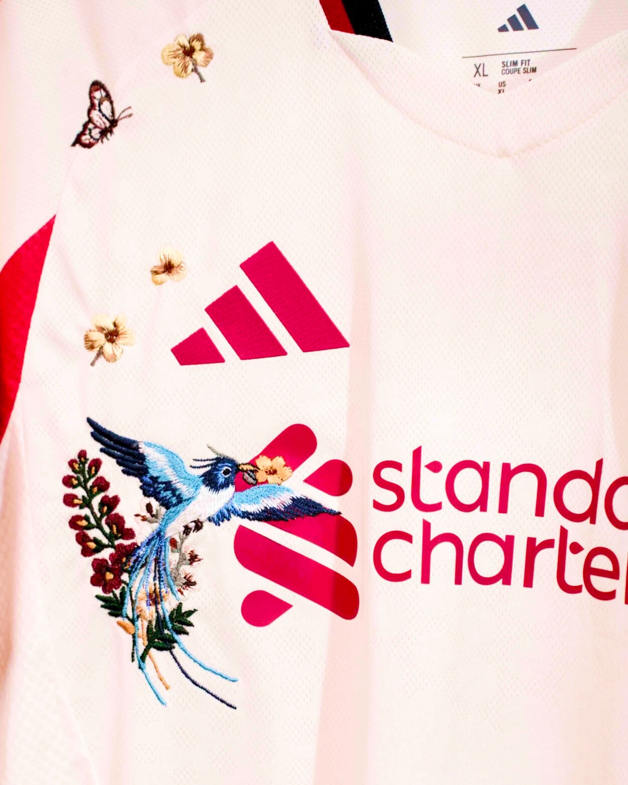 Macro Texture Shot Of The Right Chest On The Custom Embroidered White Football Shirt, Highlighting The Haptic 3D Thread Quality Of A Flying Blue Kingfisher Bird and Golden Blossoms.