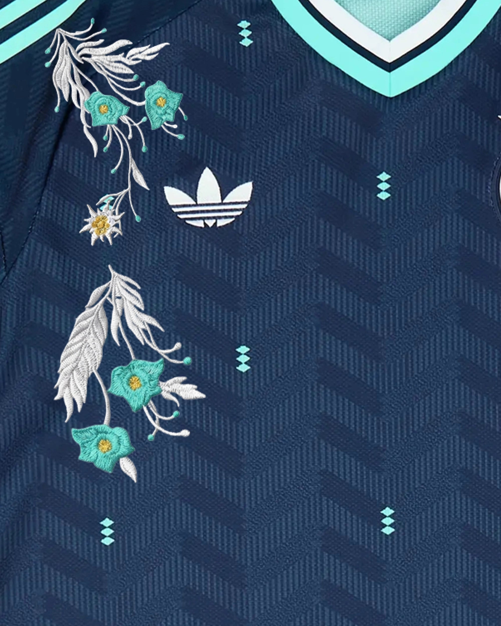 Close-Up Shot Of The Right Chest Of The Custom Germany Away Kit, Showcasing The White Trefoil Logo Intertwined With Hand-Guided Mint Green Alpine Blossoms.
