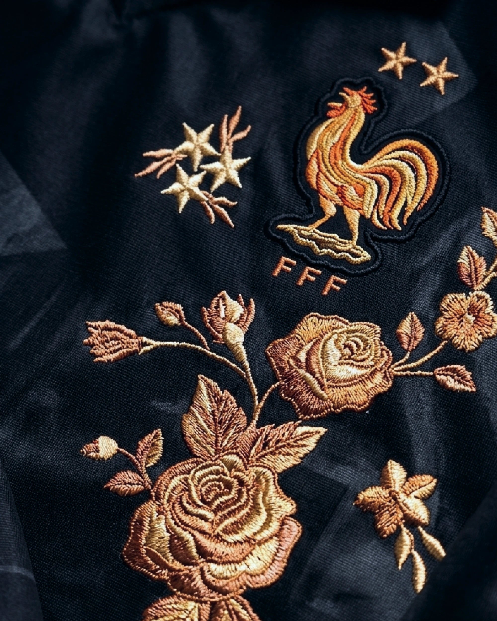 Ultra close-up hand-embroidered bronze roses in deep amber and gold thread with botanical leaves on France black concept jersey — artisanal embroidery VOLTA Paris & Versailles