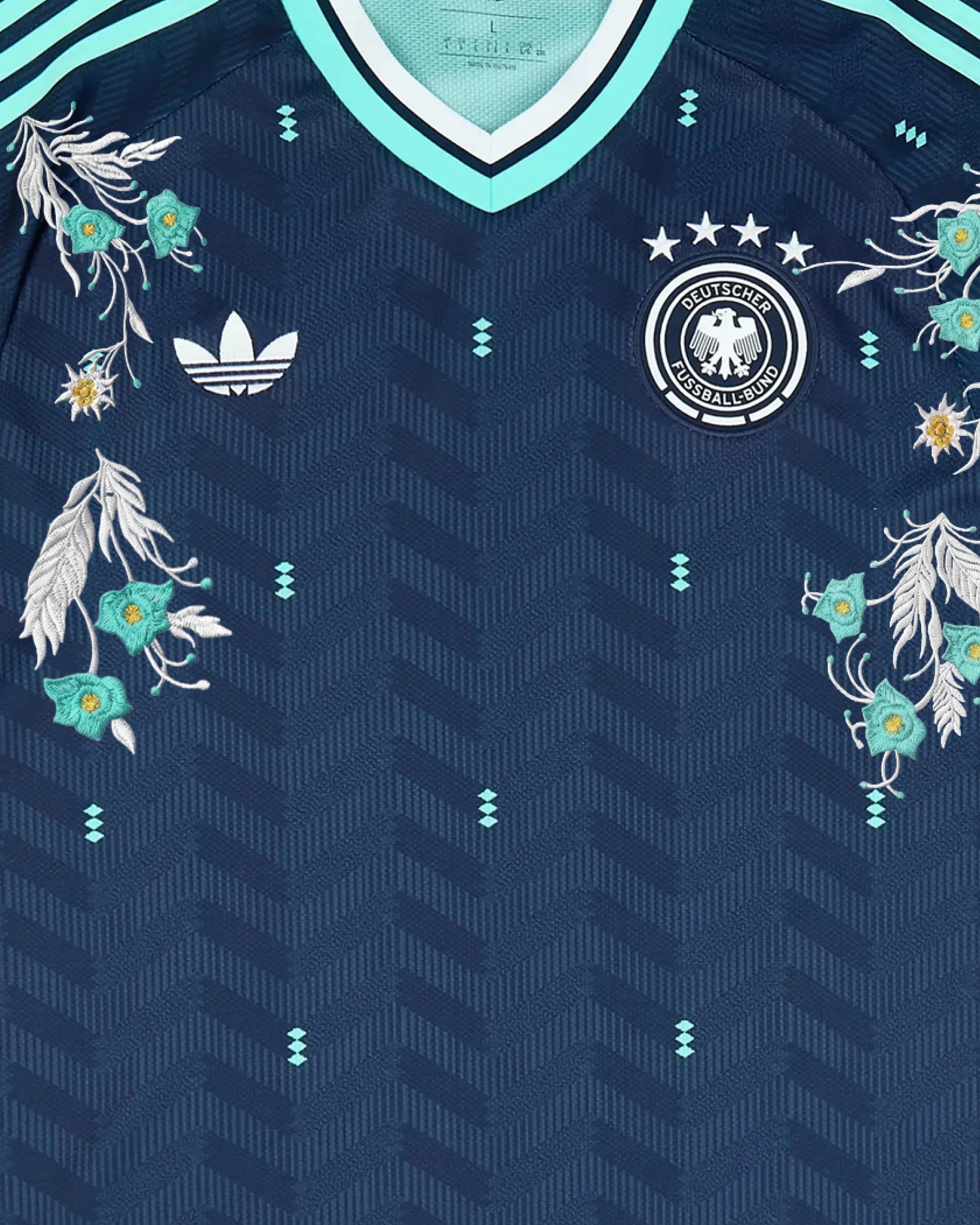 Upper Torso Centered Shot Of The Germany Embroidered Jersey 2026, Displaying The Balanced Composition of Silver Foliage and Mint Flowers Across Both Crests.
