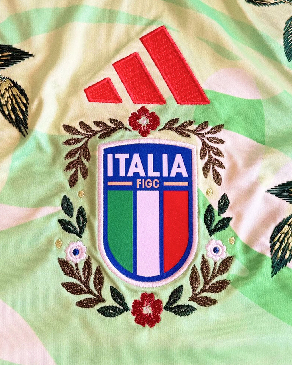 Close-Up Macro Shot Of the Center Chest On the Italy Kit Revisited, Highlighting Custom Embroidered Bronze Leaves and Crimson Flowers Encasing The Tricolour FIGC Emblem.