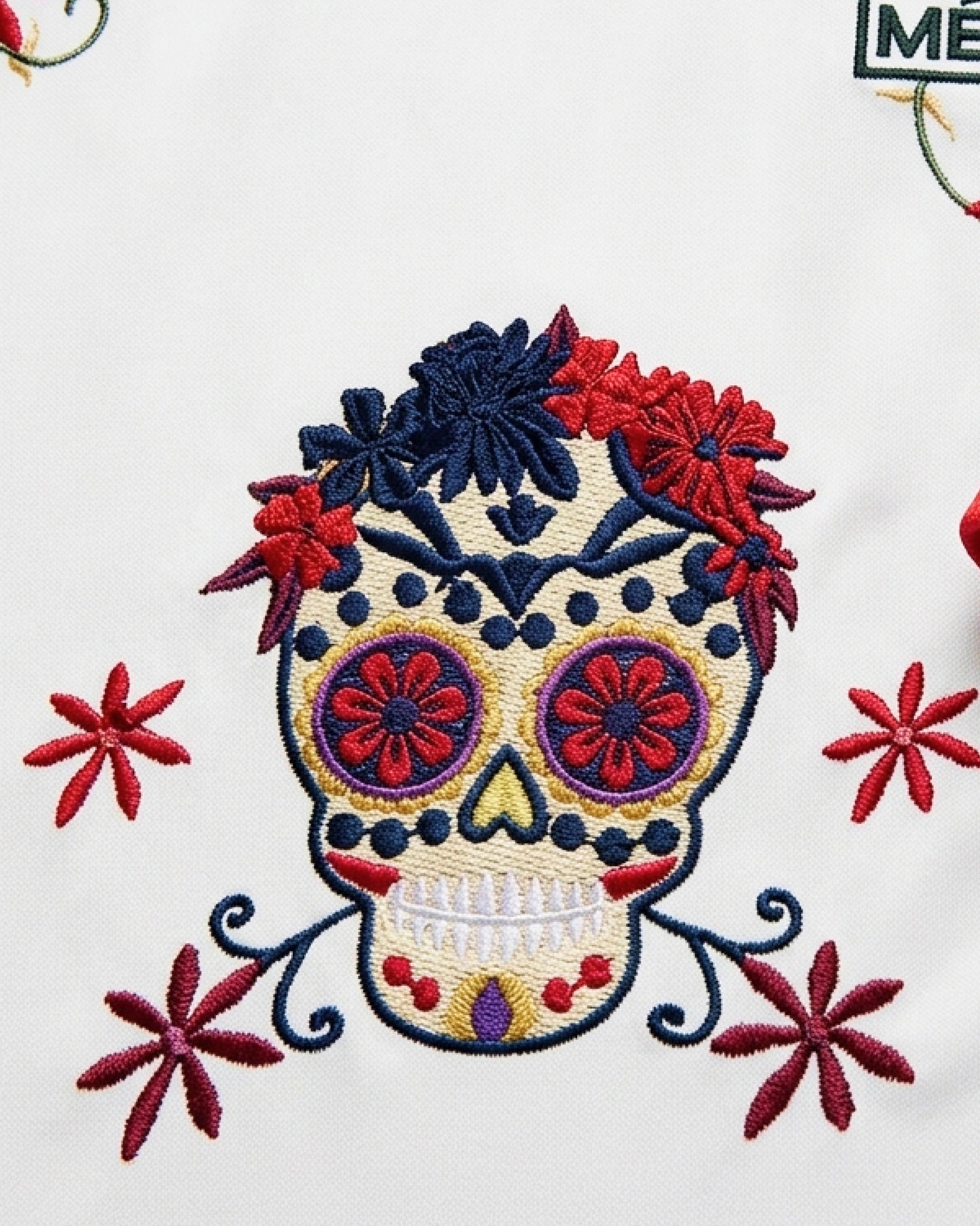 Macro Texture Shot Focusing On The Center Chest, Showcasing The Intricate Calavera Sugar Skull Embroidery With Haptic 3D Navy, Crimson, And Gold Stitching.