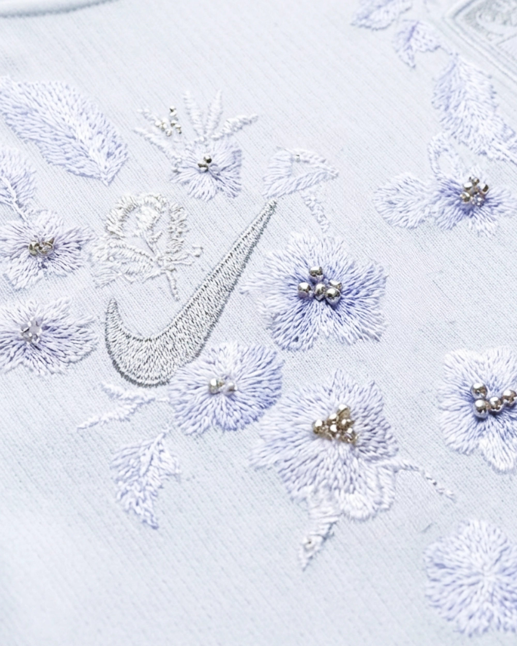 Macro detail of the artisan hand-guided embroidery on the Norway World Cup Jersey, showcasing the haptic 3D texture of silver threads and delicate hand-applied pearls mimicking frost.
