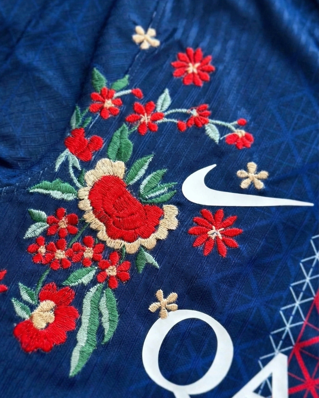 Close-up hand-embroidered red floral detail on PSG concept jersey — artisanal botanical embroidery Paris
